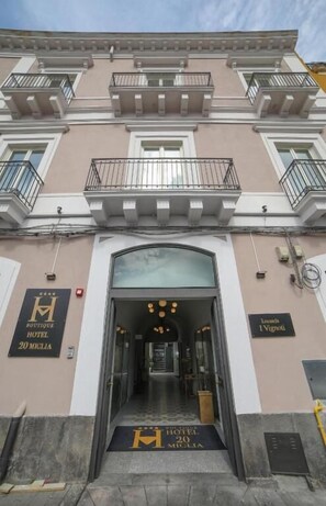 Entrada de un hotel con puertas dobles, un balcón y un cartel que indica el nombre y la dirección del hotel.