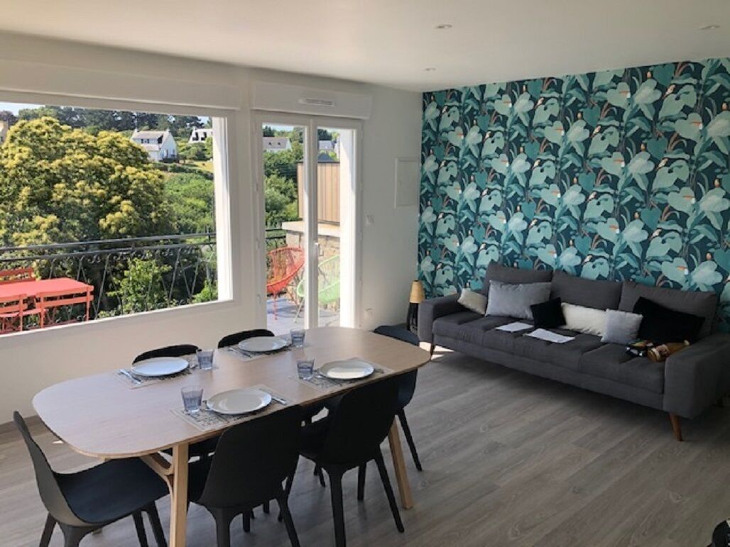 Ein modernes Wohnzimmer mit Essbereich, einem grauen Sofa und einer Wand mit Muster.