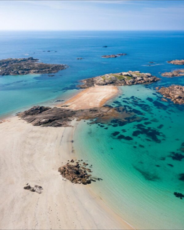 Vue aérienne d’une zone côtière avec des eaux turquoise limpides, des plages de sable et des affleurements rocheux.