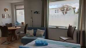 Ein modernes Zimmer mit einer Couch, Stühlen, einem kleinen Tisch und einem Bett mit blauem Handtuch.