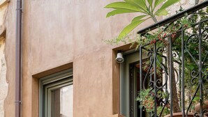 Un balcone con ringhiera in ferro battuto, un vaso con una pianta e una finestra.