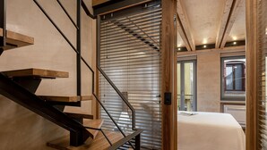 Una camera da letto moderna con una scala in legno, un letto con copriletto bianco e una finestra con persiane.