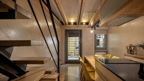 Una cucina moderna con elementi in legno, un'area pranzo con sedie gialle e una scala con gradini in legno.