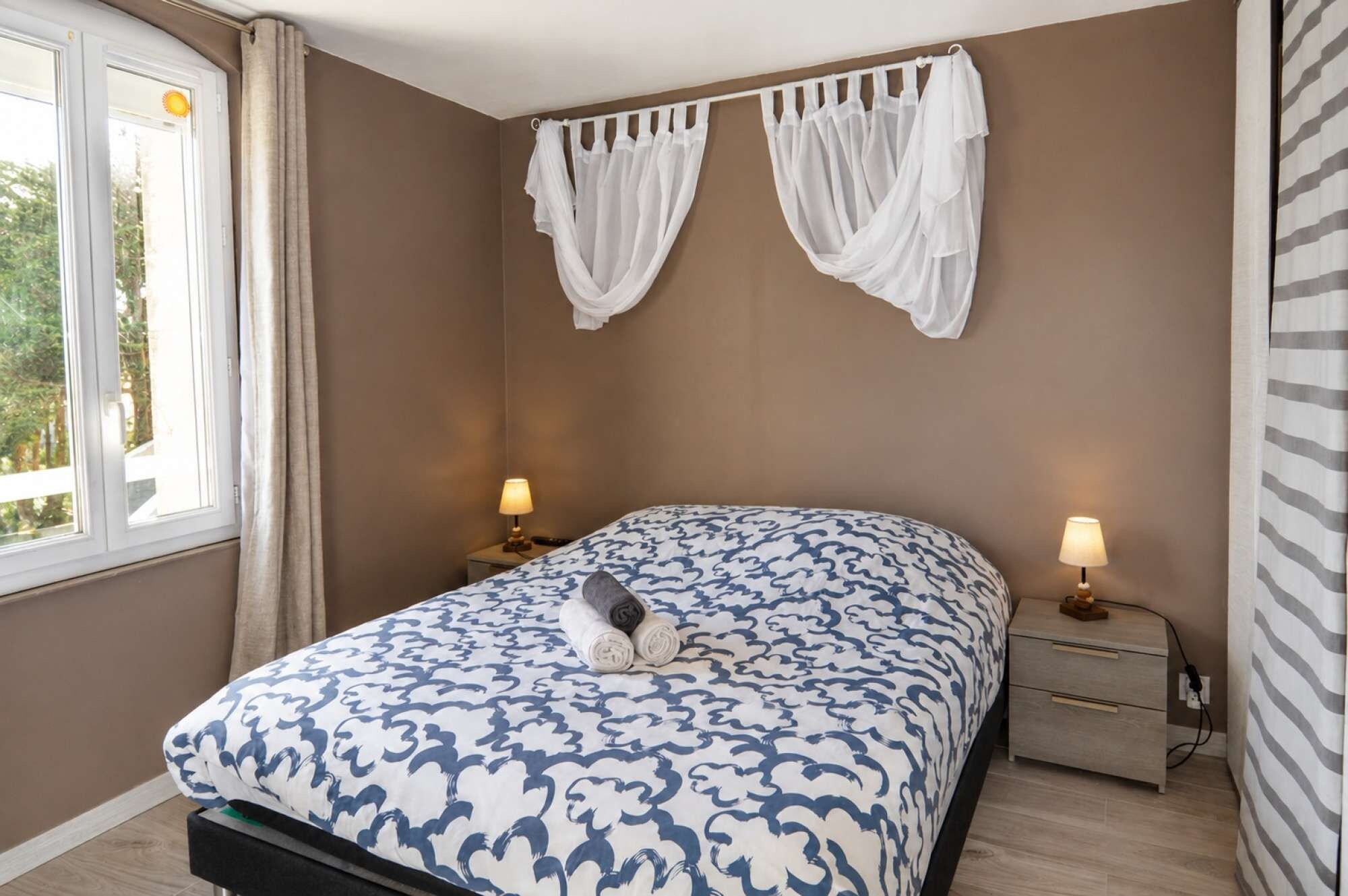 A bedroom with a bed, two bedside lamps, a window with curtains, and a wall-mounted curtain rod.