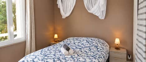 A bedroom with a bed, two bedside lamps, a window with curtains, and a wall-mounted curtain.