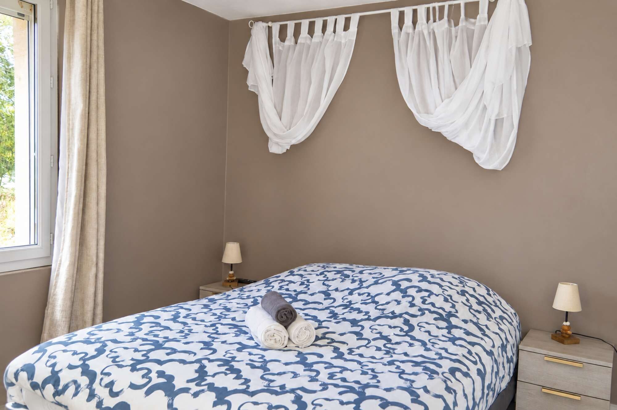 Une chambre à coucher comprenant un lit, deux tables de chevet, une fenêtre avec des rideaux et un baldaquin fixé au mur.