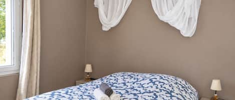 Une chambre à coucher comprenant un lit, deux tables de chevet, une fenêtre avec des rideaux et un baldaquin fixé au mur.