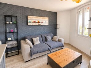 A modern living room with a grey sofa, a wooden coffee table, and a black shelving unit against a brick wall. - Apartment near port center and beach - Sea view (Courseulles-sur-Mer)