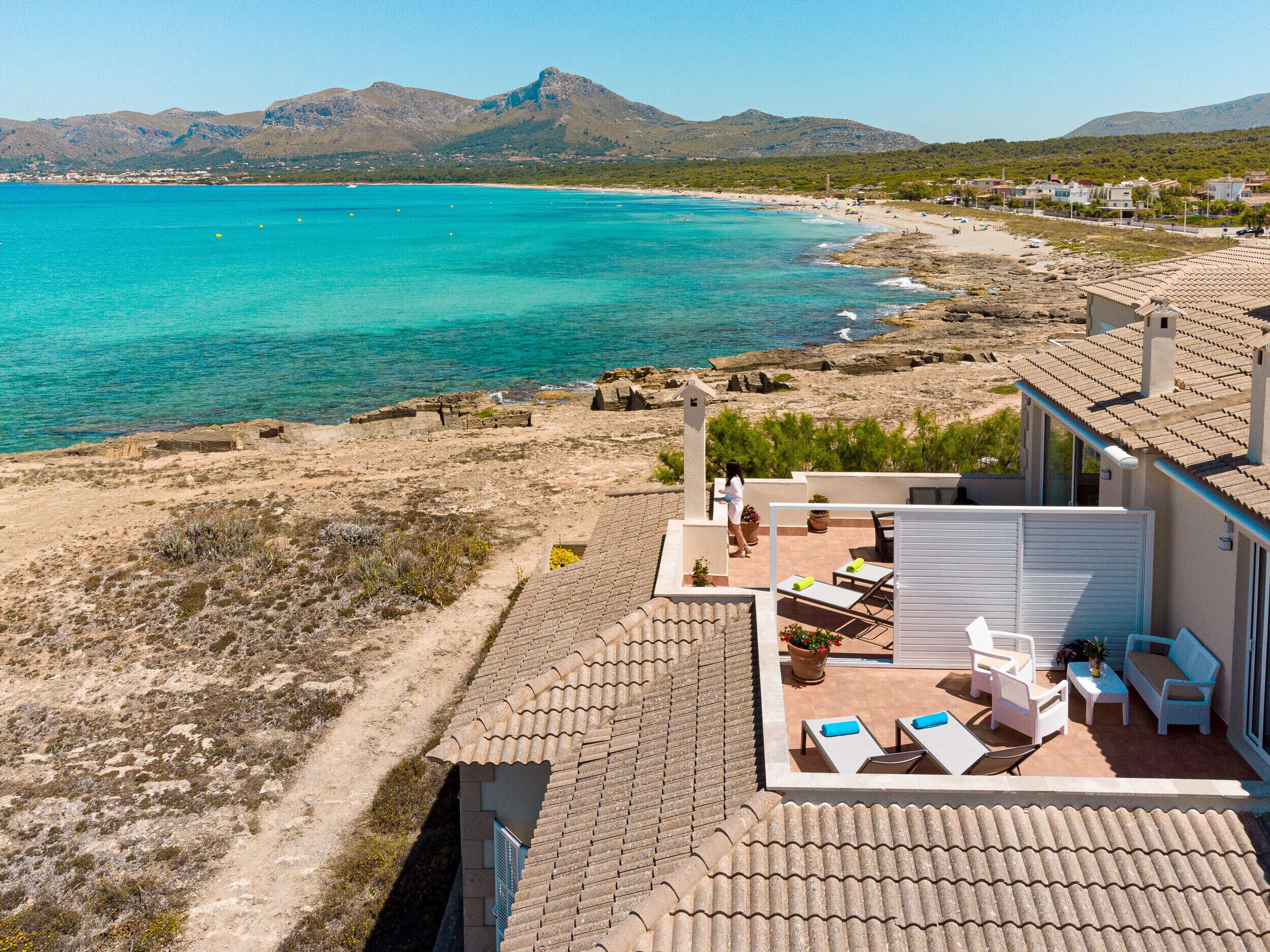 Een kustpand met een terras met uitzicht op turquoise water en een bergachtig landschap.