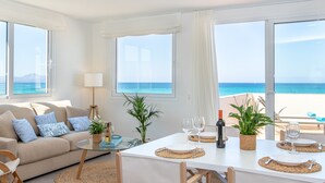 Een moderne woonkamer met een bank, eettafel en stoelen, grote ramen met uitzicht op zee en een balkon met uitzicht op het strand.