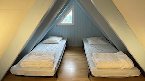 Une petite chambre mansardée avec deux lits simples et un puits de lumière.