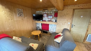 Un salon chaleureux avec deux canapés gris, une petite table en bois, un téléviseur à écran plat, une cheminée en pierre et un plafond en bois.