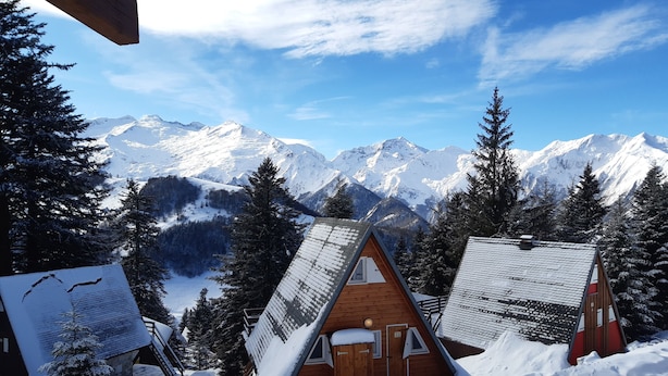 Une cabane au toit en pente, entourée d’arbres et de montagnes couverts de neige.
