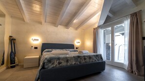 A bedroom with a bed, bedside tables, a nightstand, a window with curtains, and a view of the outside.