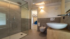 A modern bathroom with a glass shower enclosure, a freestanding sink, and a bidet.