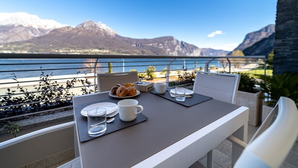 A balcony table with breakfast items, a view of a lake, and mountains in the background.