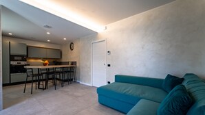 A modern living room with a teal sofa and a kitchen area with a dining table and chairs.