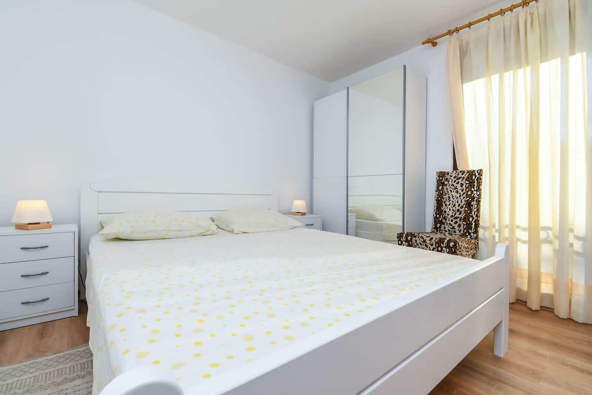 Une chambre bien rangée, avec un lit, une table de chevet, une chaise et un grand miroir.