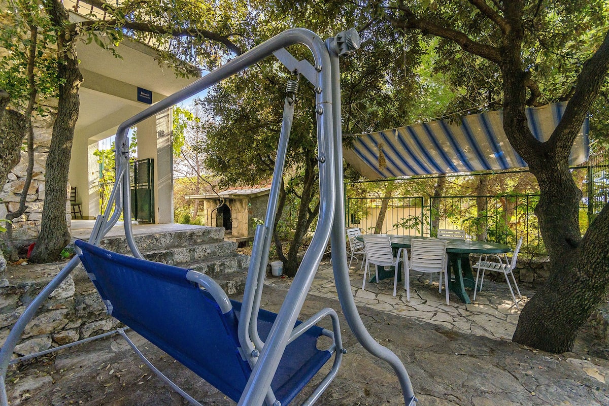 Un espace patio comprenant un fauteuil suspendu, une table avec des chaises et un coin salon couvert sous une marquise à rayures.