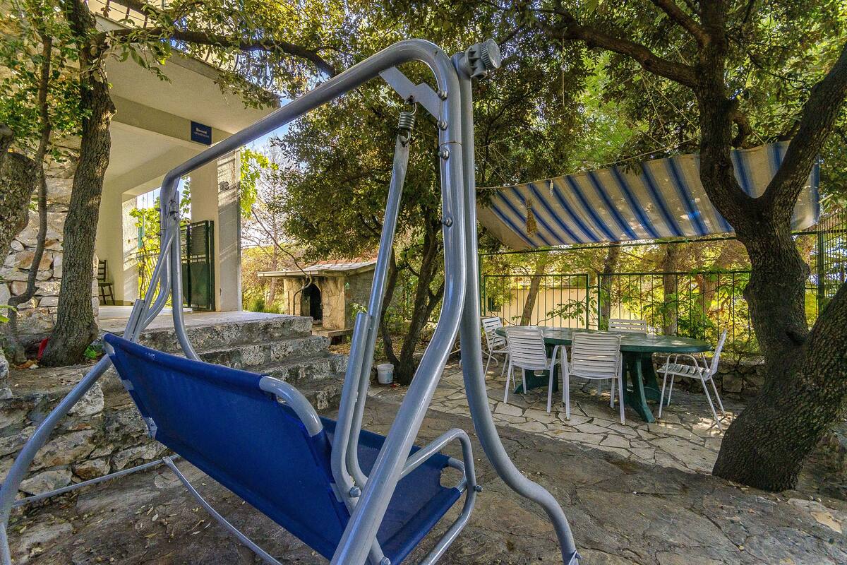 Eine Terrasse mit Schaukelstuhl, Tisch und Stühlen sowie einem überdachten Sitzbereich unter einem gestreiften Sonnensegel.