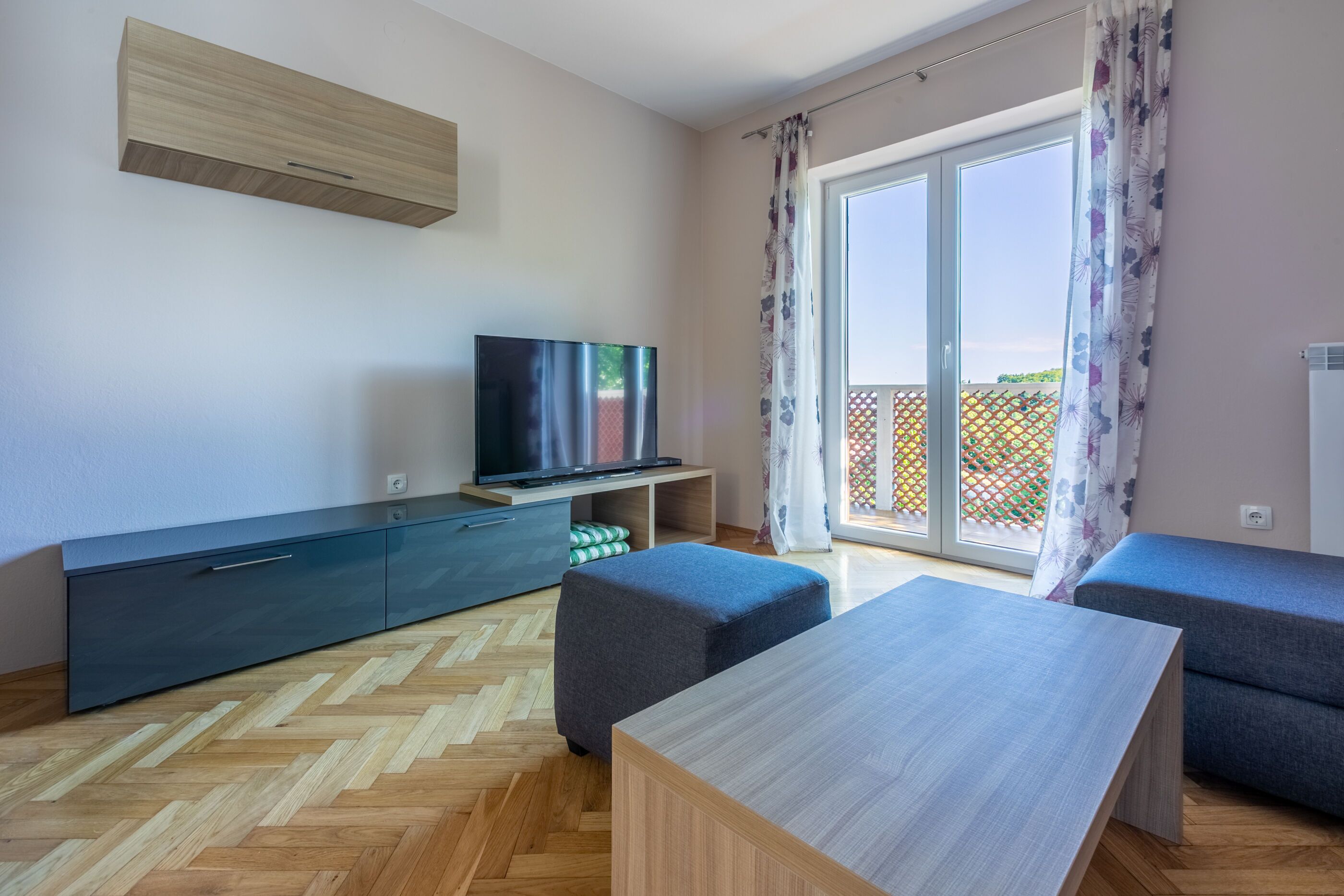 A modern living room with a TV, sofa, ottoman, and a wooden table.