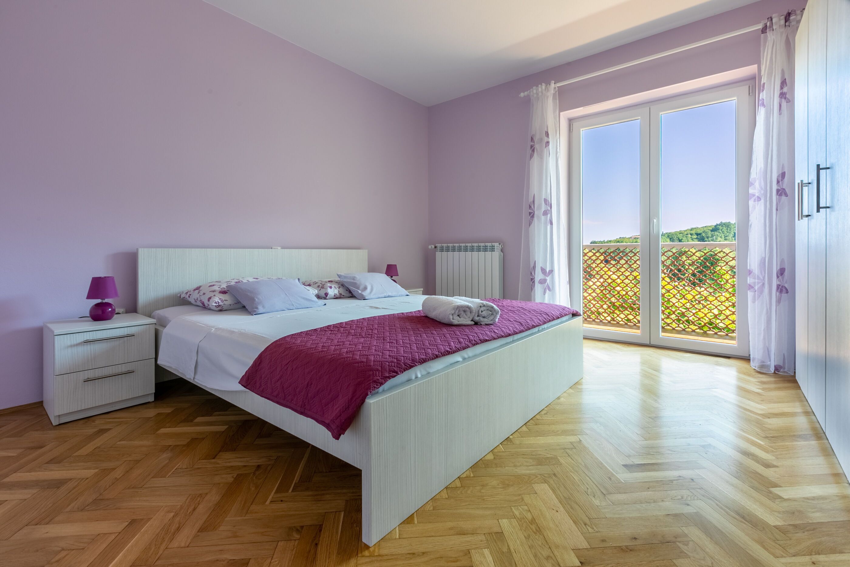 A bedroom with a bed, nightstand, and a view of a balcony.