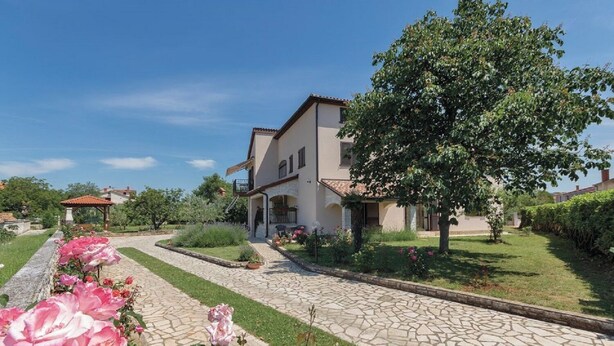Une maison à deux étages, avec un chemin de pierre menant à l’entrée, entourée de jardins bien entretenus et d’un grand arbre.