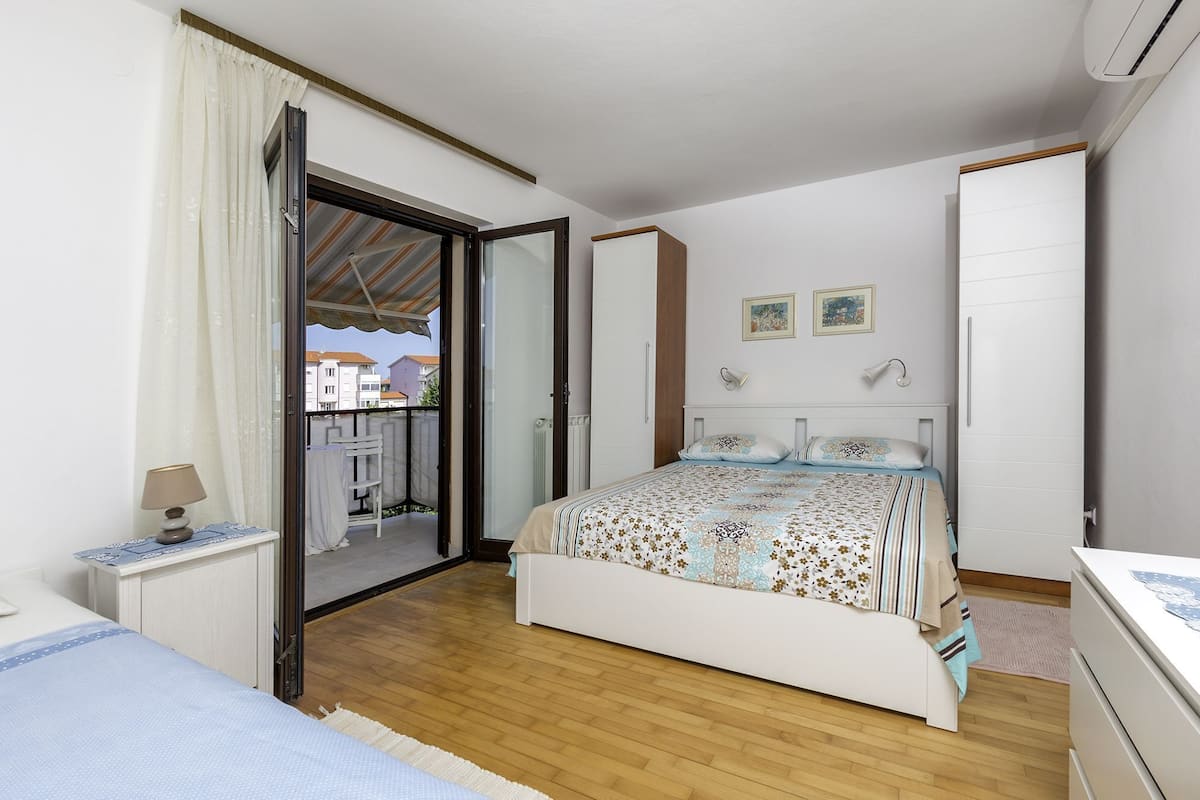 Ein Schlafzimmer mit Bett, Nachttisch, Lampe, Kleiderschrank und einer Glastür zum Balkon.