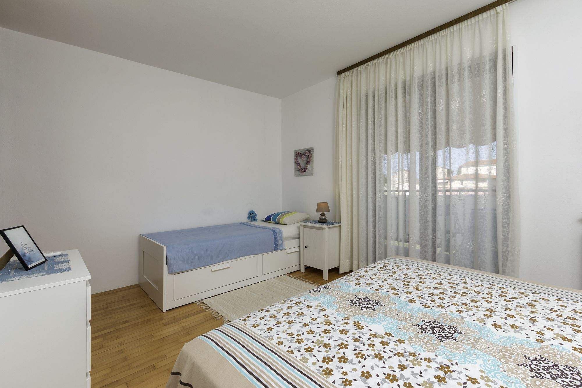 A bedroom with a single bed, a bedside table, a nightstand, a desk, and a chair.
