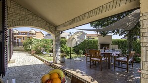 Une terrasse extérieure avec un sol en pierre, une table dressée pour le repas et un panier de fruits.