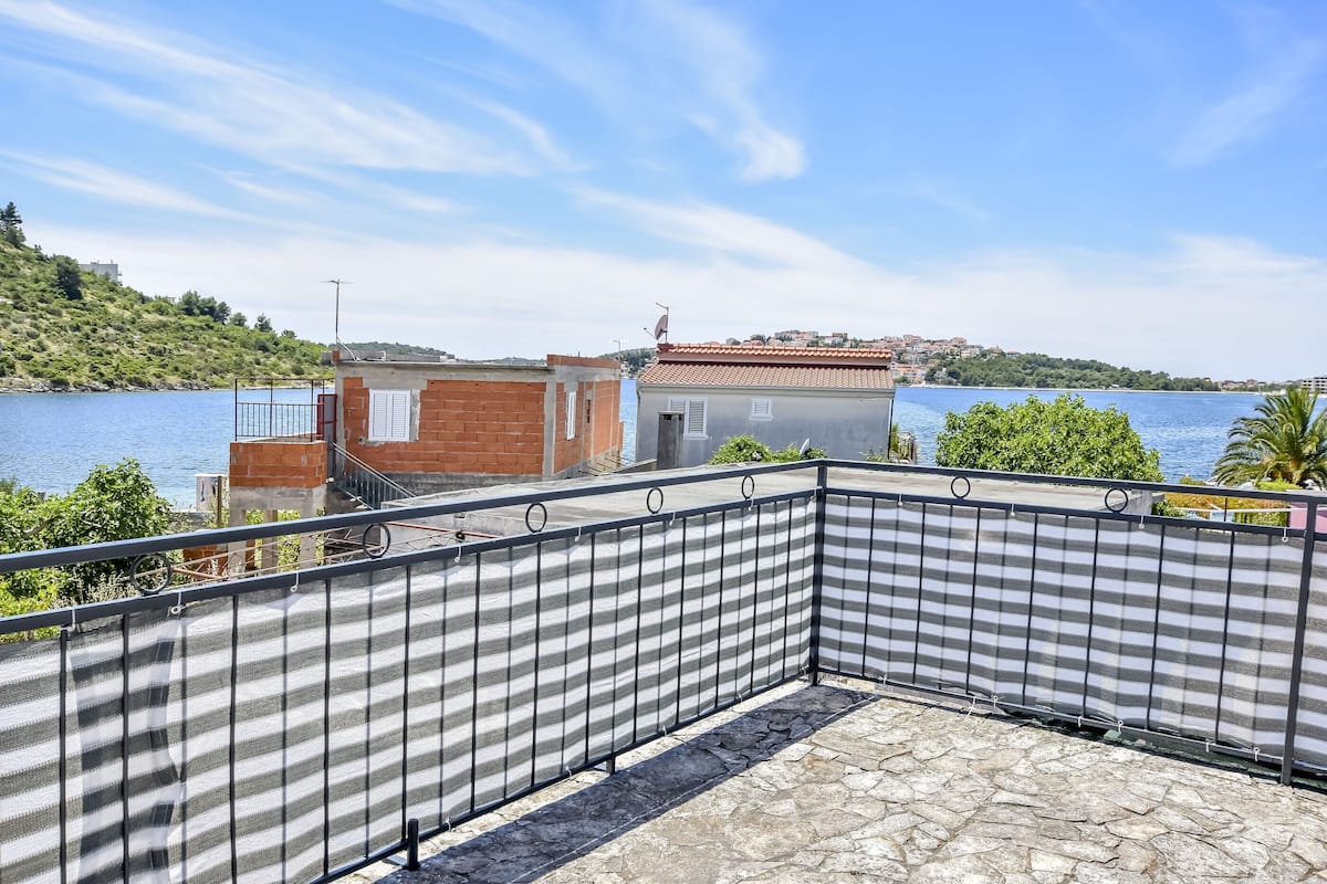 A balcony with a view of a lake, a small building with a red roof, and a stone floor.