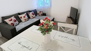 A living room with a sofa, a TV, a table with a vase of flowers, and framed pictures on the wall. - Apartments Matas (Rogoznica)