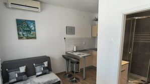 A compact living space with a sofa, a small dining table, a kitchen area, and a shower. - Apartments Matas (Rogoznica)
