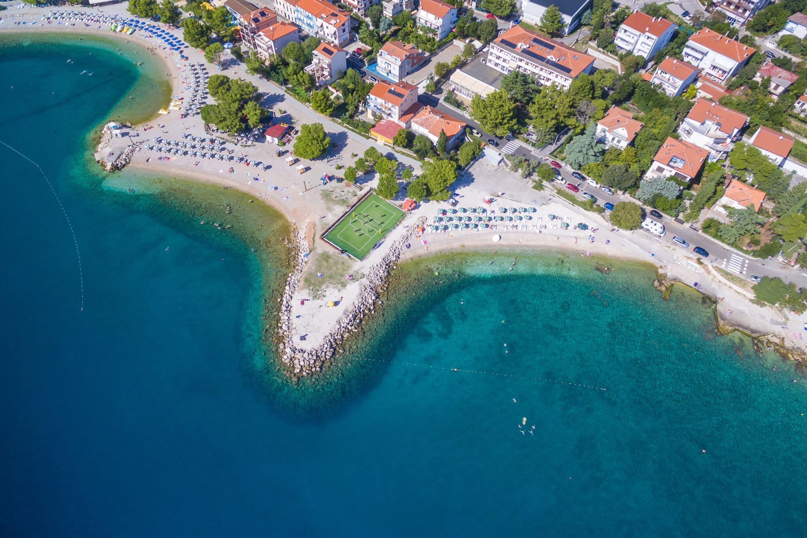 Vue aérienne d’une zone côtière avec une plage, des eaux cristallines et des immeubles résidentiels.