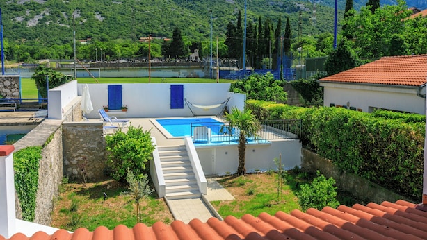 Ein Poolbereich mit Bergblick, eine Treppe, die zu einem Pool führt, und ein weißes Gebäude mit rotem Dach.