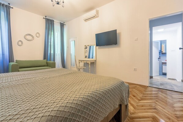 Une chambre à coucher avec un lit, un canapé vert, une télévision et une salle de bain visible à travers une porte ouverte.