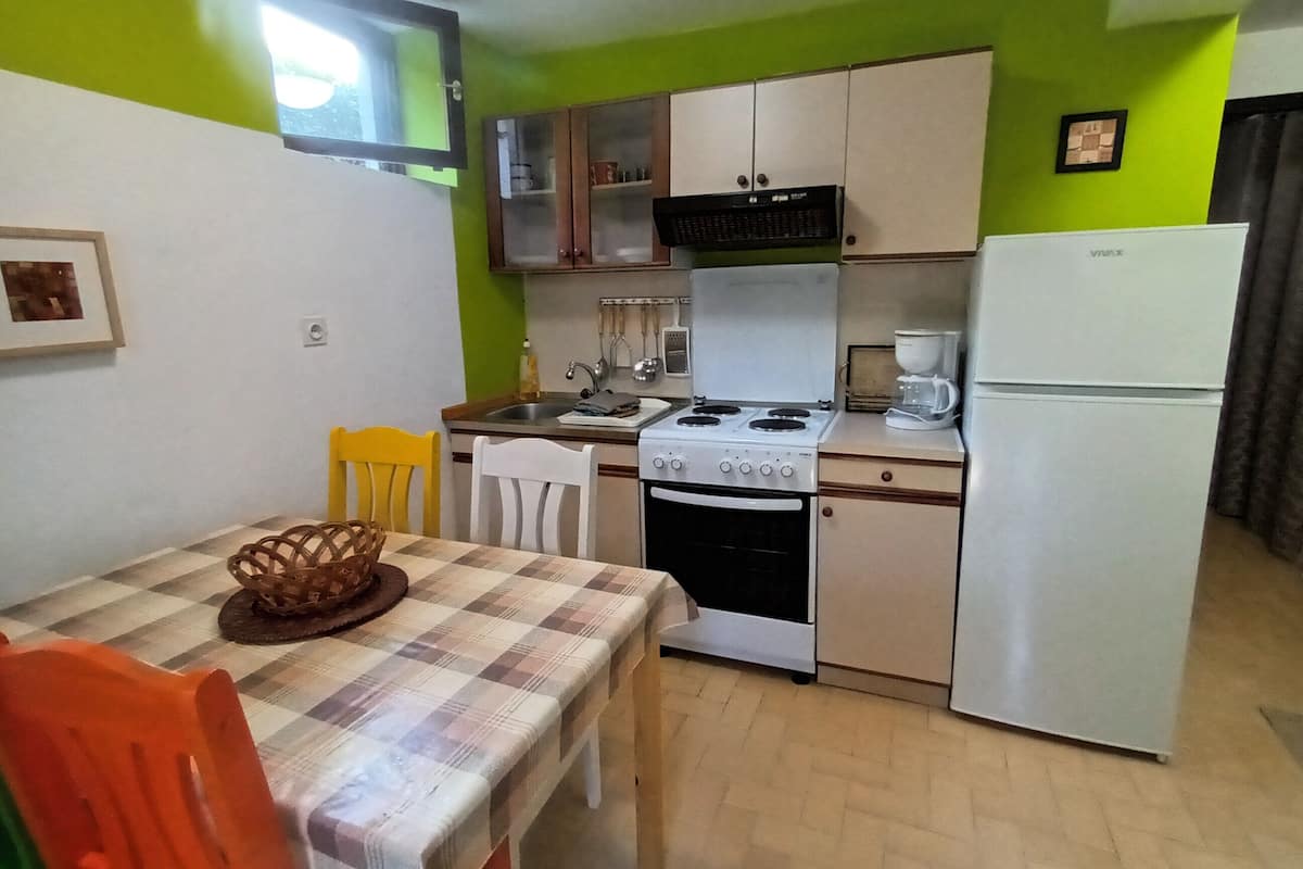A compact kitchen with a stove, oven, and refrigerator, a dining table with chairs, and a window above the sink.