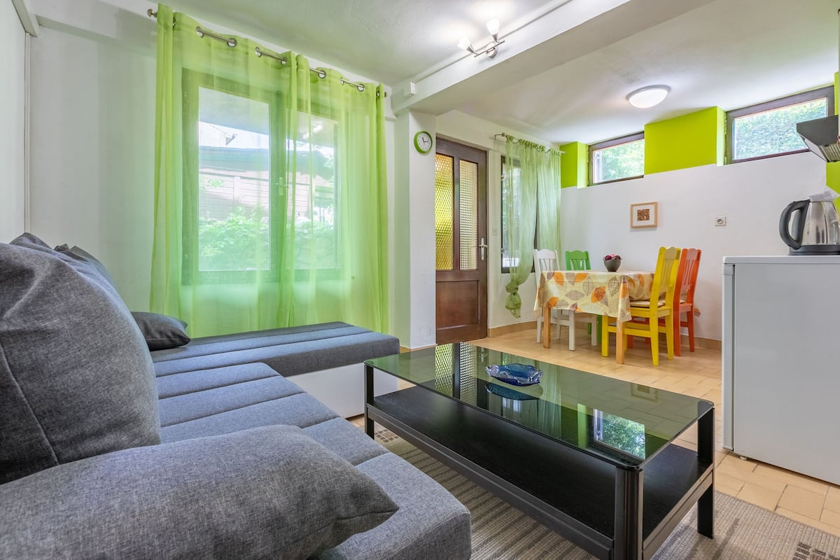 A living room with a grey sofa, a glass coffee table, and a dining area with a table and chairs.