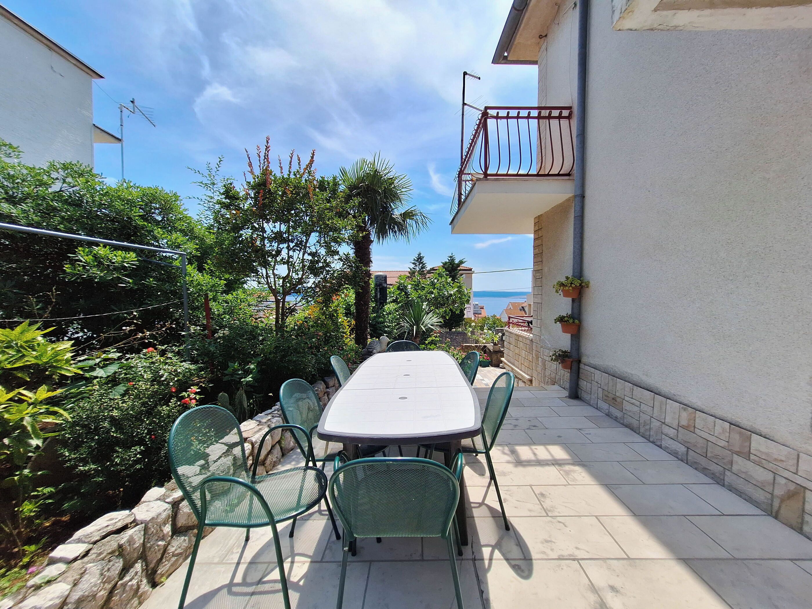 A patio with a table and chairs, surrounded by greenery and a view of the sea.
