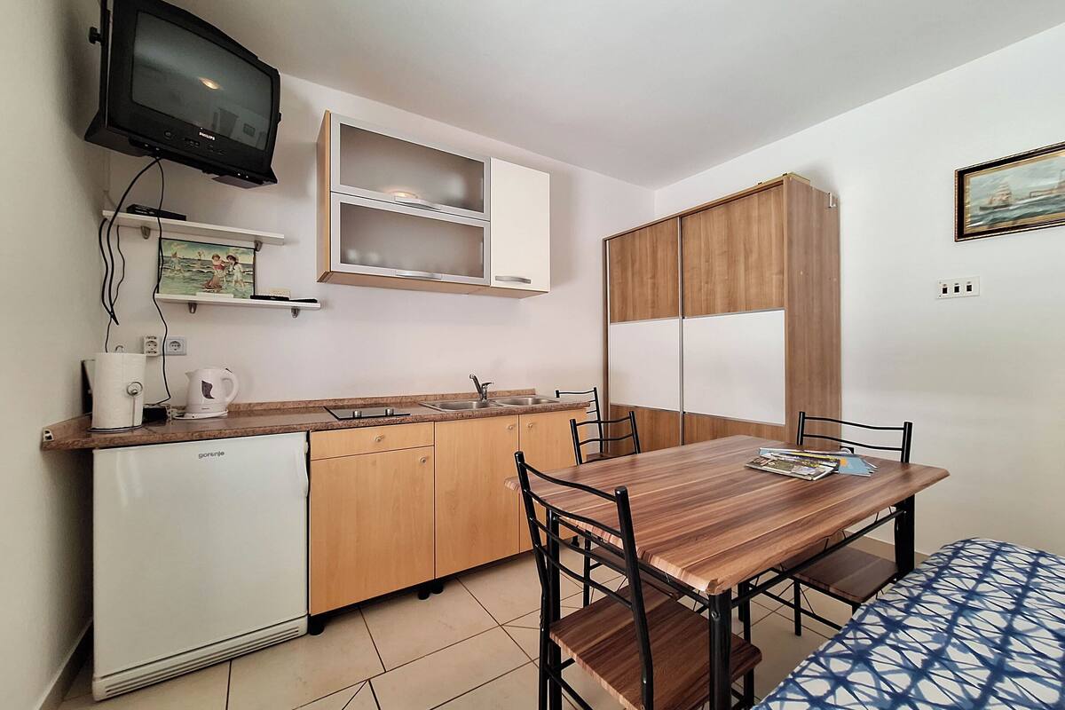 A compact kitchen with a wooden table and chairs, a built-in oven, and a television mounted on the wall.