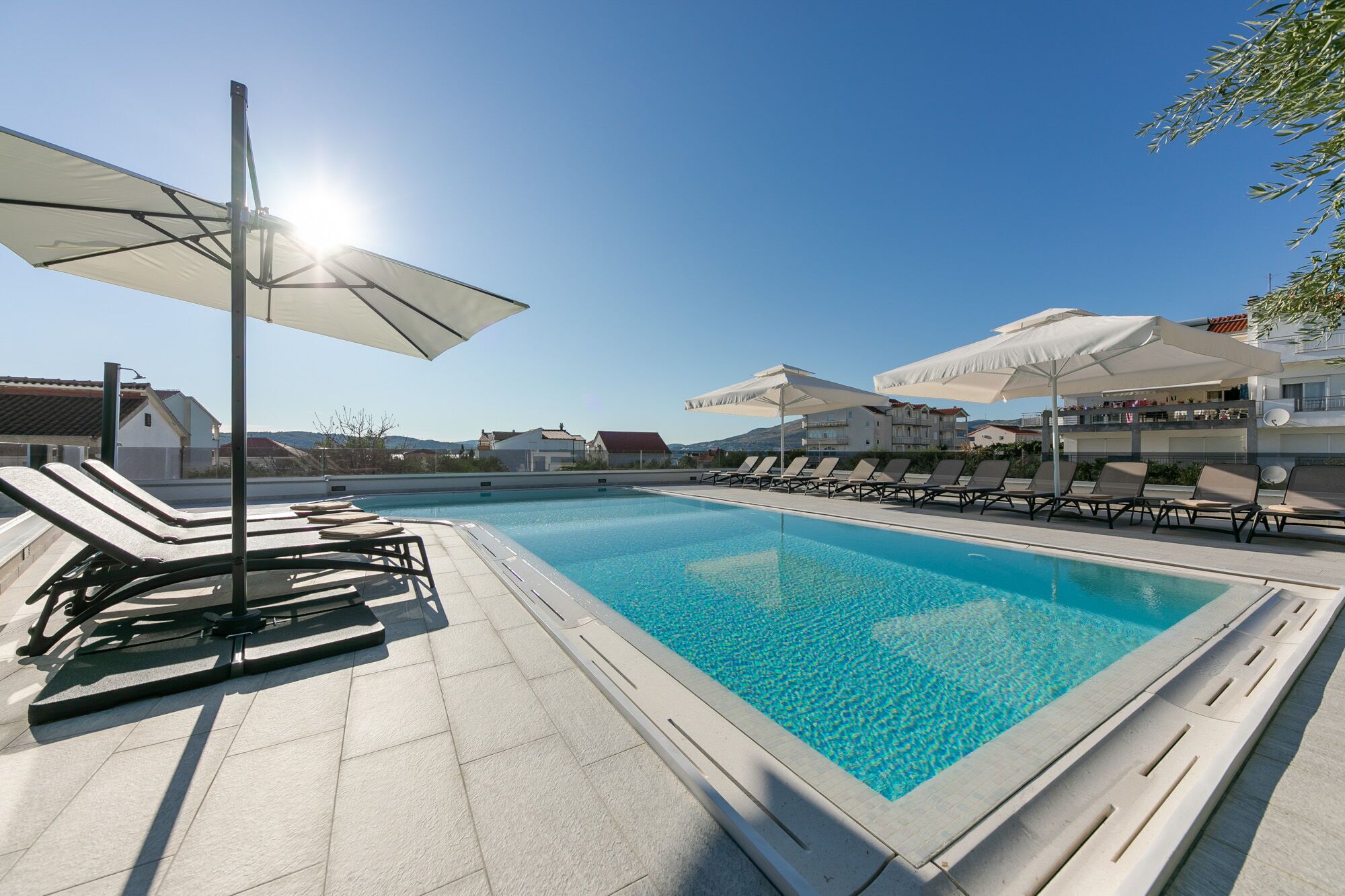 A swimming pool with lounge chairs and umbrellas, surrounded by buildings.