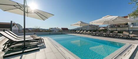 A swimming pool with lounge chairs and umbrellas, surrounded by buildings.