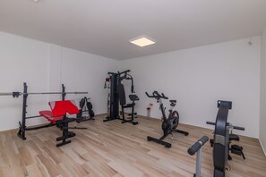 A gym with various exercise equipment including a bench press, a squat rack, and an elliptical machine. - Apartments Dora (Okrug Gornji)