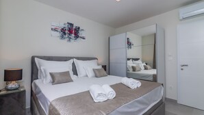 A modern bedroom with a large bed, a bedside table with a lamp, a mirror, and a wardrobe. - Apartments Dora (Okrug Gornji)