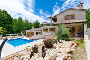 A stone house with a swimming pool, outdoor furniture, and a garden with rocks and plants. - Villa Histra (Sumber)