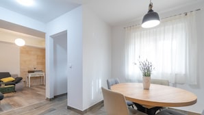 A modern dining area with a round wooden table, grey upholstered chairs, and a potted plant. - Villa Strikina Kuca (Slivno)