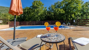 A poolside area with a tiled deck, lounge chairs, a table with drinks, and a pool. - Villa Strikina Kuca (Slivno)