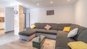 A modern living room with a sectional sofa, a coffee table, and a brick accent wall. - Villa Strikina Kuca (Slivno)