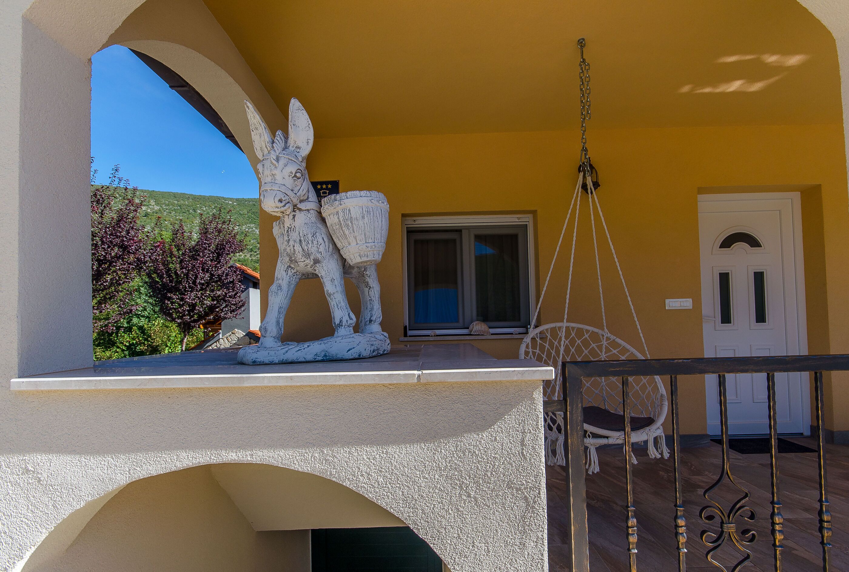 A balcony with a white donkey sculpture, a hanging chair, and a door with a window.