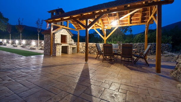 An outdoor patio with stone flooring, wooden pergola, and stone building with a chimney. - Villa Strikina Kuca (Slivno)